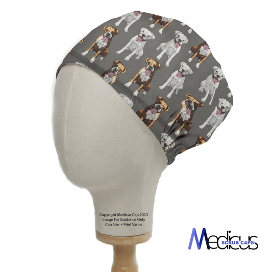 A white mannequin head displays the Dog Breeds Boxers Grey Scrub Cap by Medicus Scrub Caps, featuring various colorful dog breeds on a gray background with an adjustable fit and the brand logo in the bottom right corner.