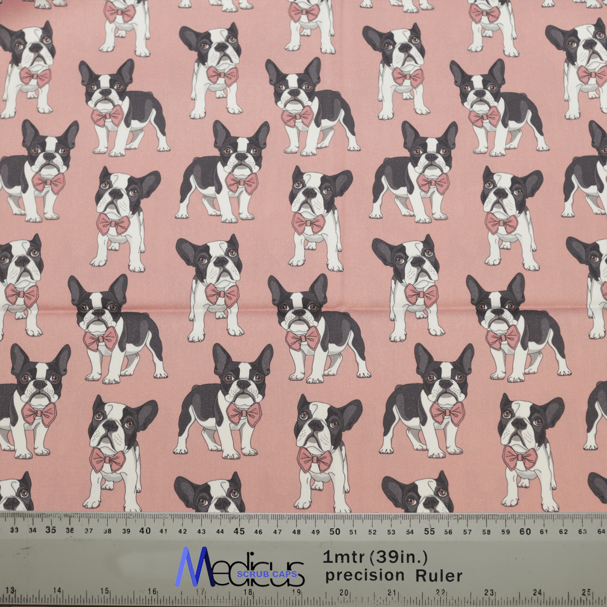The Dog Breeds French Bulldog Salmon Pink Scrub Cap from Medicus Scrub Caps features rows of black and white French bulldogs with pink bows on a pink backdrop, ideal for eco-friendly scrub caps. A ruler in the image shows approximately 1 meter of this charming design.