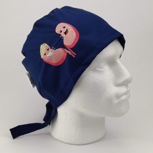 Displayed on a white mannequin head, the Medicus Scrub Caps Embroidery - Kidneys features a navy blue scrub cap with a whimsical design of two kidneys: one holding a tablet, the other a glass.