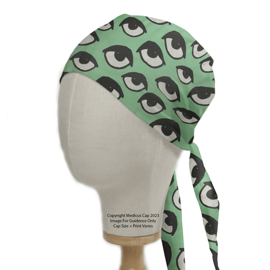 A mannequin head displays the Eyes Teal Scrub Cap by Medicus Scrub Caps, featuring a black and white eyes pattern. The cap ties at the back and reads Copyright Medicus Cap 2023 Image For Guidance Only Cap Size + Print Varies, adding a unique touch to any medical uniform.