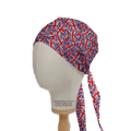 A mannequin head wears a Flag UK Scrub Cap by Medicus Scrub Caps, adorned with vibrant overlapping Union Jack flags. The cap features two long ties at the back and is made from eco-friendly materials for comfort, with a fabric label reading Copyright Medicus Caps 2022.