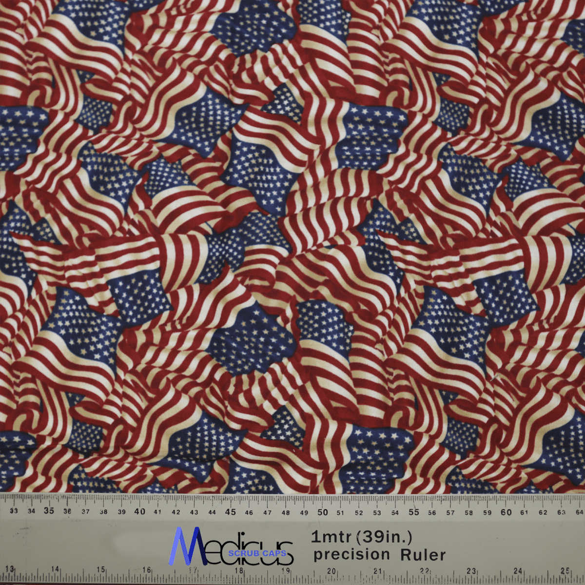 The Flag USA Scrub Cap by Medicus Scrub Caps features a vibrant pattern of overlapping U.S. flags in red, white, and blue, embodying patriotic pride. It includes a ruler at the bottom for measurements in inches and centimeters, adding practicality.