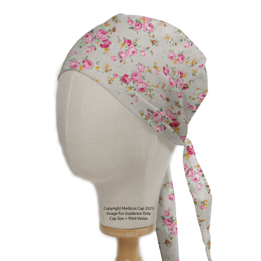 The Medicus Scrub Caps Floral Bunches Roses Grey Scrub Cap features pink roses on a light grey background, displayed on a mannequin head with tie-back fastening.