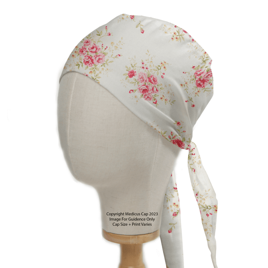 A Medicus Scrub Caps mannequin displays the Floral Flower Arrangement Roses White Scrub Cap, featuring pink and green floral patterns. The cap is tied at the back, with noted copyright information and details about size and print variations.