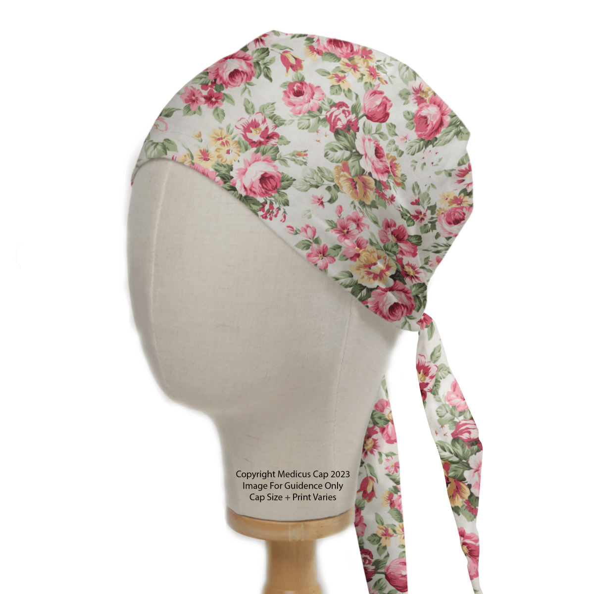 The Medicus Scrub Caps Floral Large Roses Vintage Ivory Scrub Cap, featuring a delightful pink and yellow floral pattern on white, is stylishly displayed on a mannequin. Tied back for adjustability, it offers an eco-friendly, sustainable choice for medical professionals.