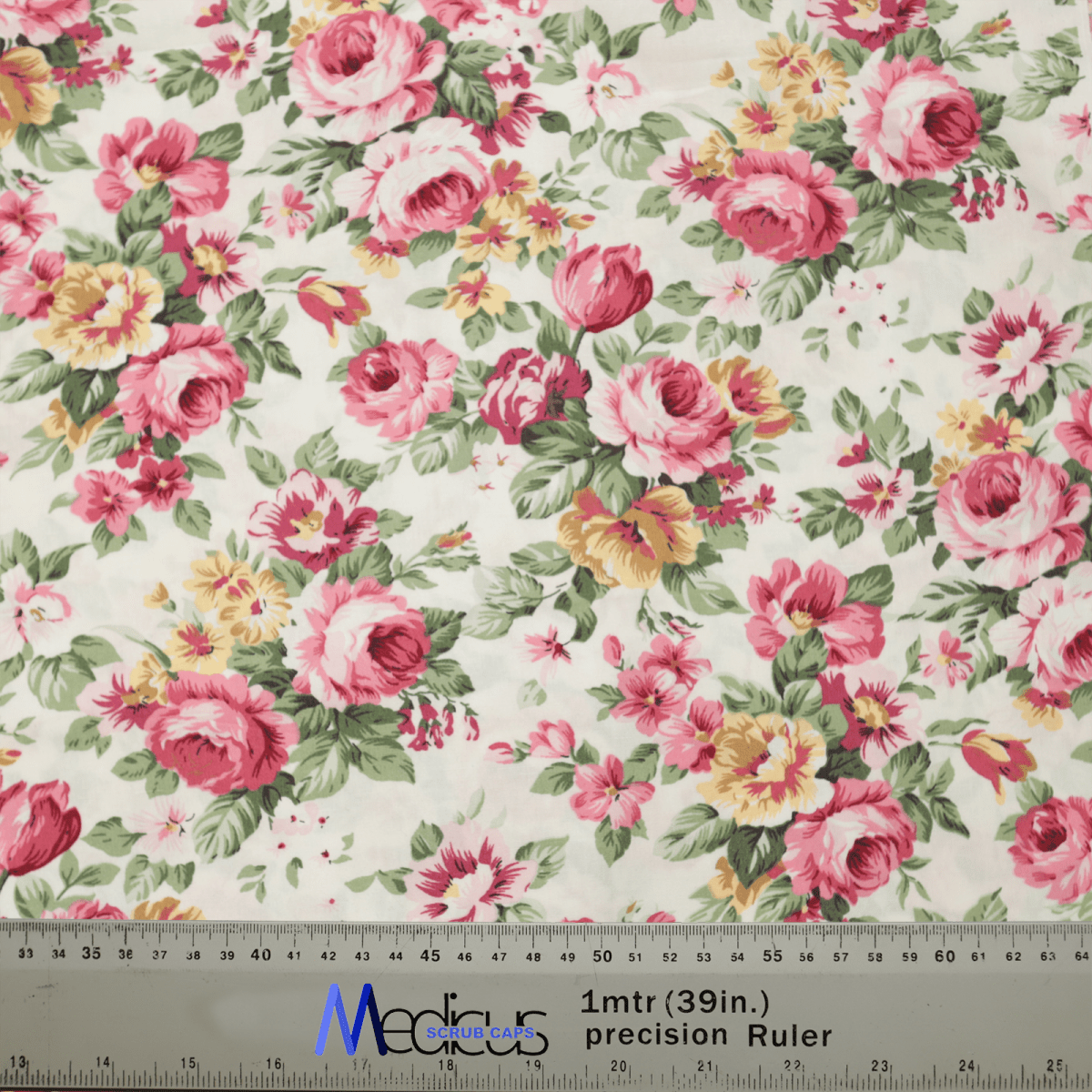 The Medicus Scrub Caps Floral Large Roses Vintage Ivory Scrub Cap features pink, yellow, and white roses with green leaves on a light backdrop. A transparent ruler at the bottom measures in centimeters and inches, labeled Medocasa, ideal for crafting a vintage ivory scrub cap.