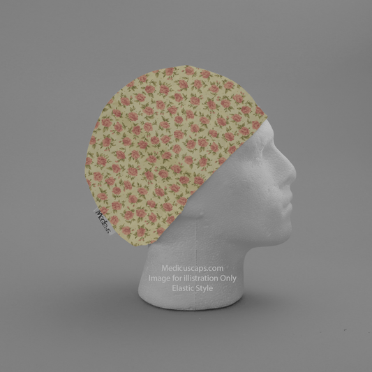 A mannequin head features the Medicus Scrub Caps Floral Mini Roses Pink Scrub Cap, showcasing a floral pattern of pink roses on light yellow. This sustainable scrub hat includes a small tag on the edge and is displayed on a plain gray backdrop.