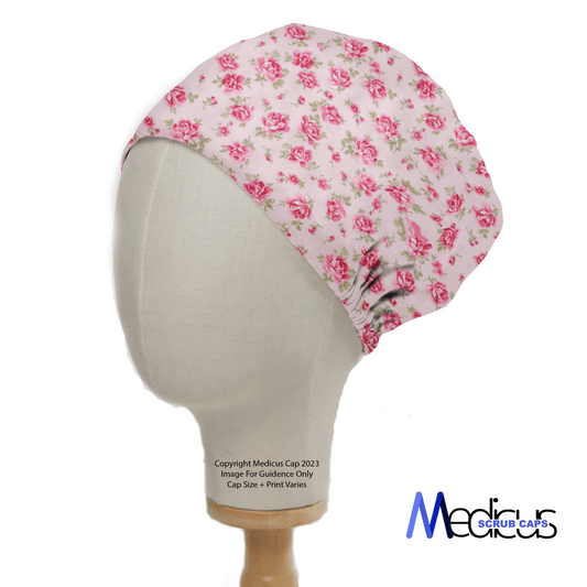 A mannequin head displays the Floral Pink On Baby Pink Scrub Cap, celebrated for its superior fit. It features a pink floral pattern on a white background, with Medicus Scrub Caps partially visible in the lower right corner, making it ideal for medical professionals.