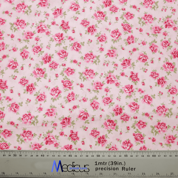 The Floral Pink On Baby Pink Scrub Cap by Medicus Scrub Caps features pink roses with green leaves on white fabric. Ideal for medical professionals, it includes a ruler at the bottom for precise measurements in centimeters and inches, blending style and functionality.