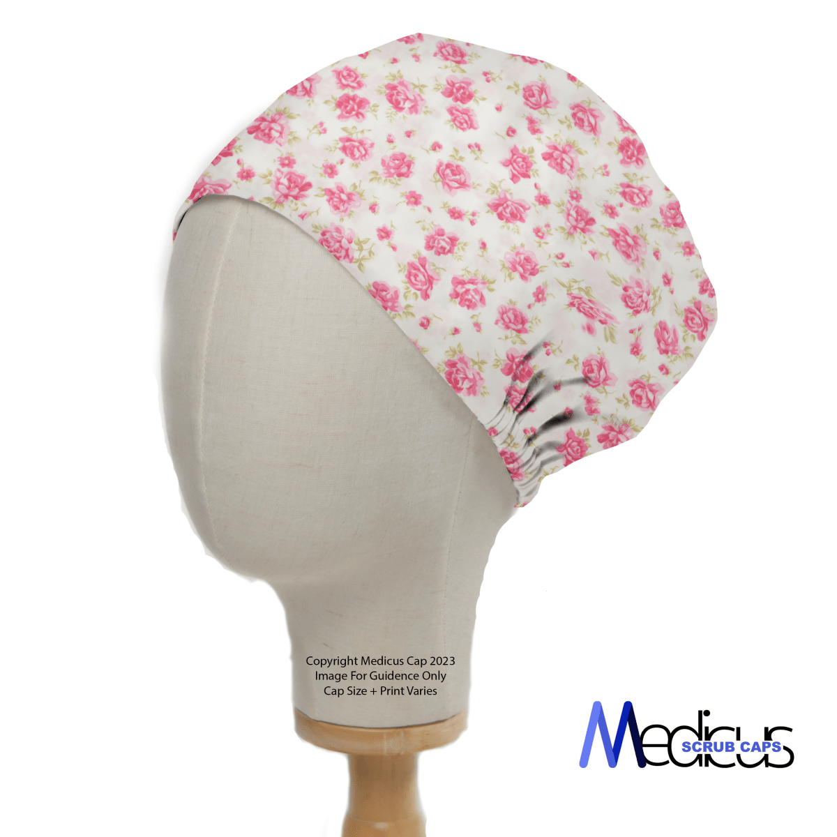 A mannequin head displays the Floral Pink On Ivory Scrub Cap by Medicus Scrub Caps, featuring a pink floral rose design. The logo Medicus Scrub Caps at the bottom right emphasizes their commitment to sustainable healthcare.