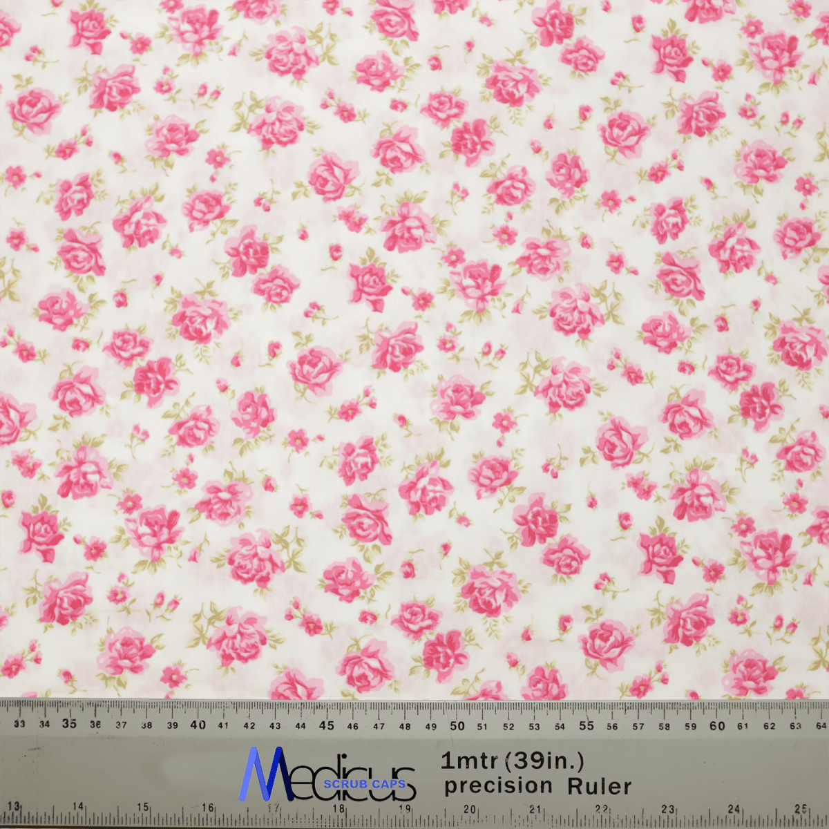 The Floral Pink On Ivory Scrub Cap by Medicus Scrub Caps showcases a delicate pattern of small pink roses on an ivory background. A gray ruler at the bottom displays dimensions in both centimeters and inches, making it perfect for crafting elegant, sustainable healthcare essentials.