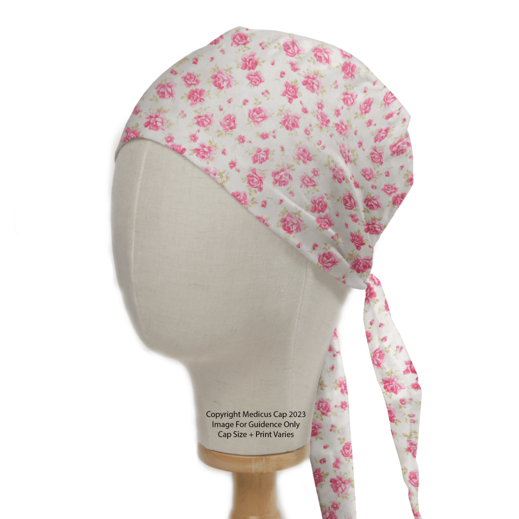 A mannequin head showcases the Floral Pink On Ivory Scrub Cap by Medicus Scrub Caps, featuring vibrant pink roses on an ivory base. Tied at the back, this reusable cap is ideal for medical professionals dedicated to sustainable healthcare.