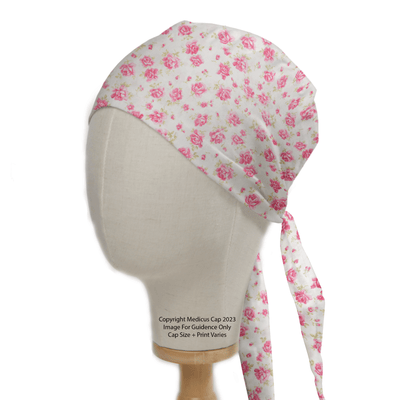 A mannequin head showcases the Floral Pink On Ivory Scrub Cap by Medicus Scrub Caps, featuring vibrant pink roses on an ivory base. Tied at the back, this reusable cap is ideal for medical professionals dedicated to sustainable healthcare.