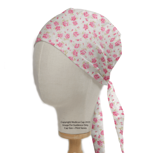 A mannequin head showcases the Floral Pink On Ivory Scrub Cap by Medicus Scrub Caps, featuring vibrant pink roses on an ivory base. Tied at the back, this reusable cap is ideal for medical professionals dedicated to sustainable healthcare.