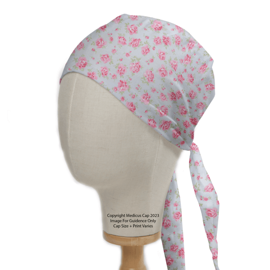 A head mannequin displays the eco-friendly Medicus Scrub Caps Floral Roses Small On Blue Scrub Cap, in light blue with a floral rose pattern and tied straps hanging elegantly at the back.