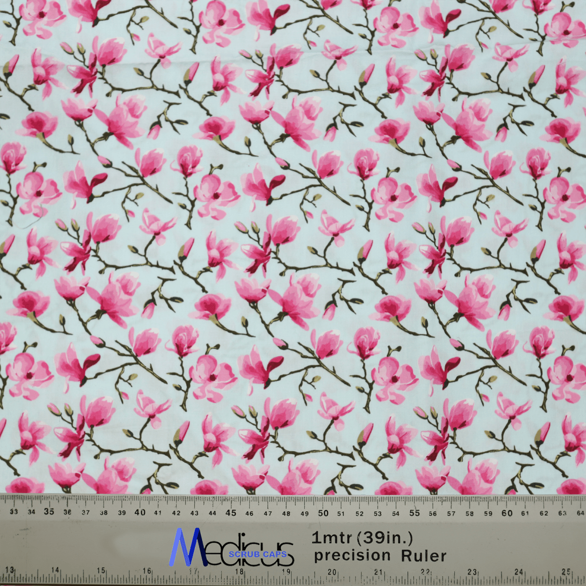 The Floral Tree Blossom Scrub Cap by Medicus Scrub Caps features pink magnolia flowers and branches on a light background, perfect for healthcare professionals. Displayed with a ruler at the bottom, it shows measurements in inches and centimeters.