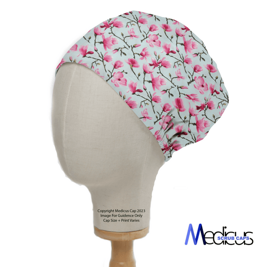 The Floral Tree Blossom Scrub Cap from Medicus Scrub Caps, displayed on a mannequin head, features pink flowers and green leaves on a white background. This classic design is perfect for healthcare professionals, with the brands logo elegantly placed at the bottom right corner.