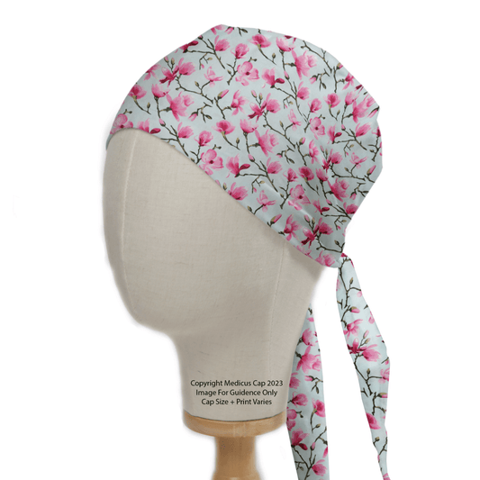 The Floral Tree Blossom Scrub Cap by Medicus Scrub Caps is elegantly displayed on a mannequin. Featuring a pink floral print and tie-back design, this essential accessory offers healthcare professionals delicate tree blossom decorations on a light background.