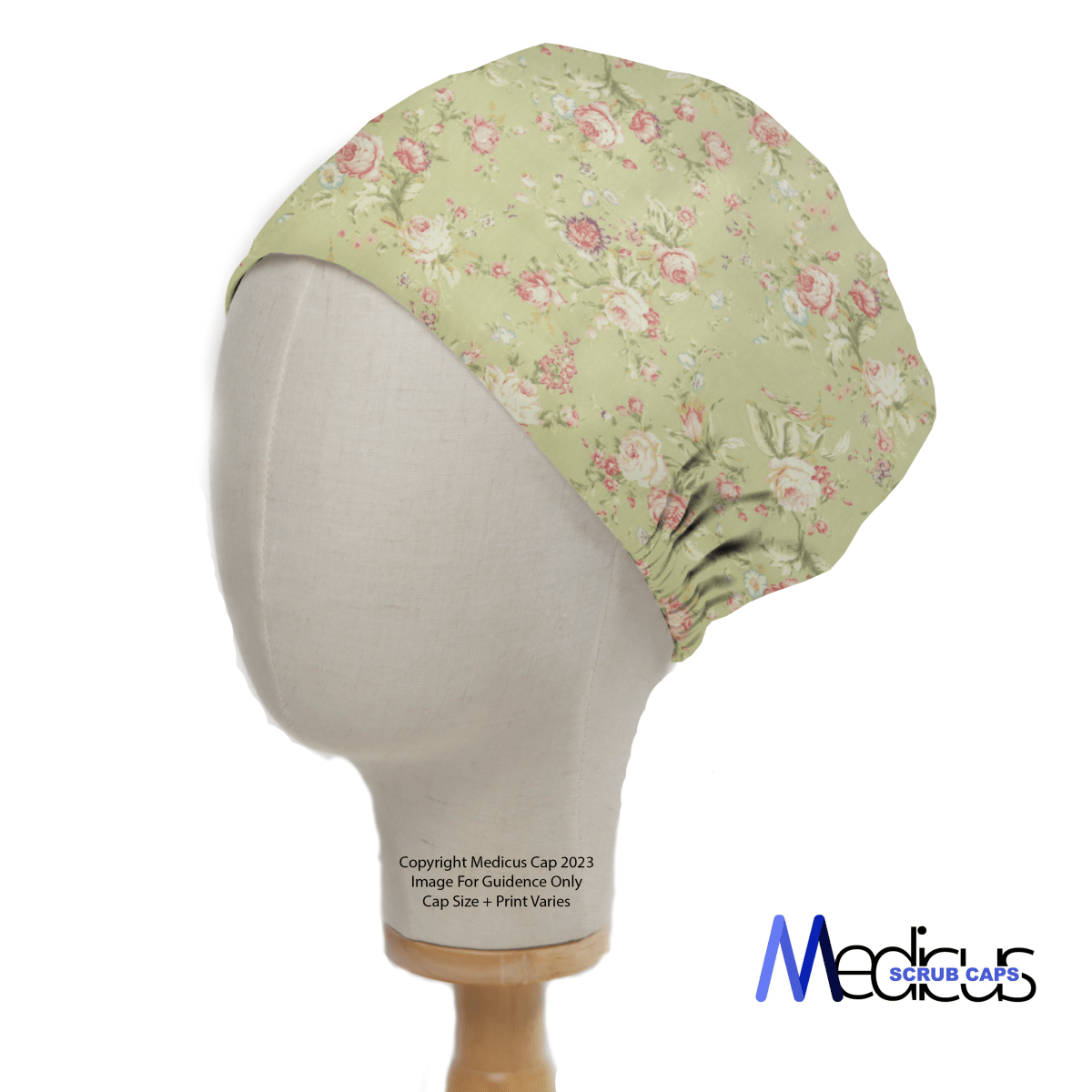 A mannequin head displays the Floral Vintage Faded Green Scrub Cap from Medicus Scrub Caps, featuring pink roses on a light green background. Designed for healthcare professionals, it offers full coverage with the brands logo on the bottom right corner.