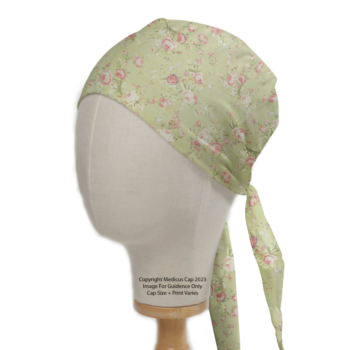 A mannequin head displays the Medicus Scrub Caps Floral Vintage Faded Green Scrub Cap, featuring pink and white blooms. Elegantly tied at the back, it has a soft, silky texture perfect for healthcare professionals who prioritize style and comfort.