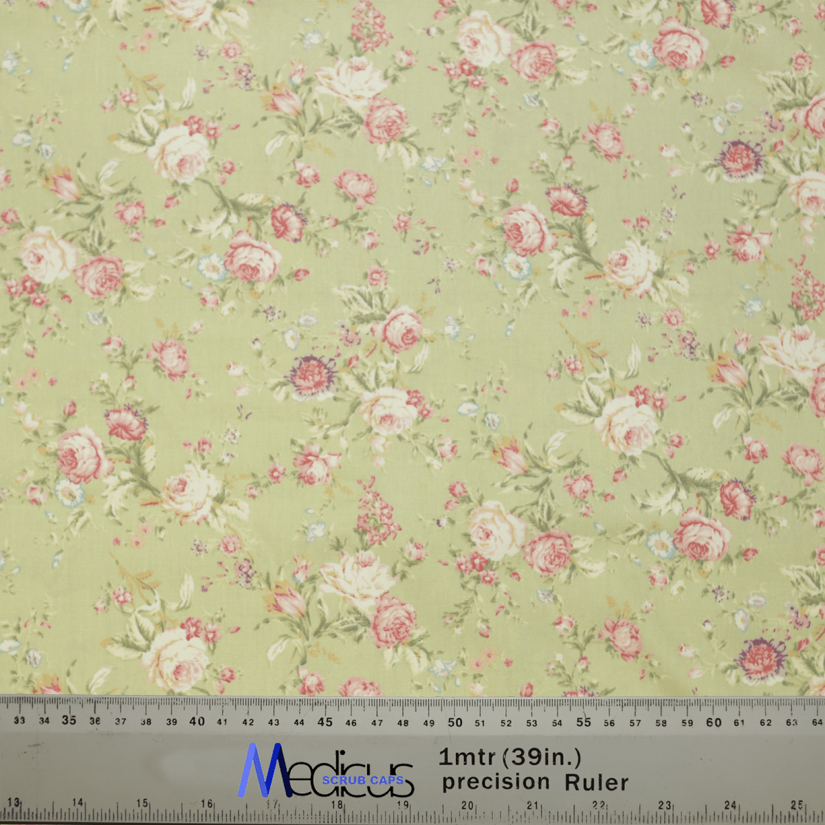 The Floral Vintage Faded Green Scrub Cap by Medicus Scrub Caps showcases pink and red roses, small white flowers, and green leaves on a pale green background. Perfect for healthcare professionals, it includes a ruler at the bottom with centimeters and inches for scale.