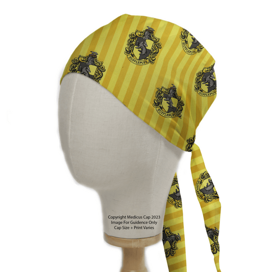 A mannequin head displays a Harry Potter Hufflepuff Scrub Cap by Medicus Scrub Caps, featuring yellow fabric with black and gray crests and animals, Hufflepuff in stripes, and eco-friendly long ends perfect for sustainable fashion fans.