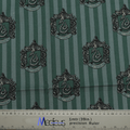 Green fabric with vertical stripes displays Slytherin crests and custom embroidery, each featuring a serpent and decorative elements. An eco-friendly ruler with metric/inch markings is seen at the bottom, ideal for designing the Harry Potter Slytherin Scrub Cap by Medicus Scrub Caps.