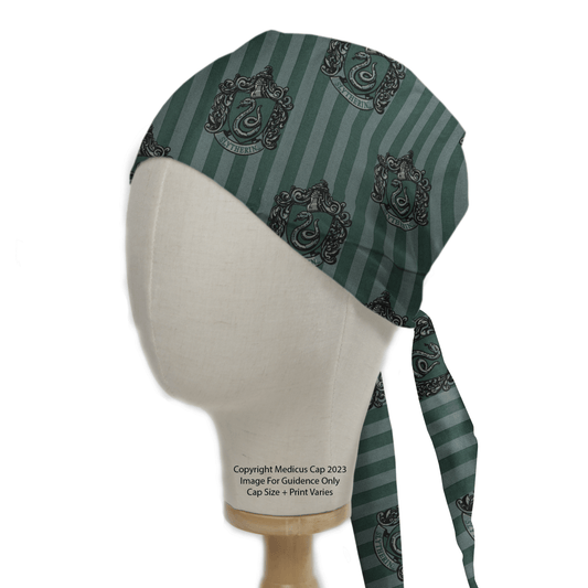 The Harry Potter Slytherin Scrub Cap by Medicus Scrub Caps is showcased on a mannequin, featuring custom embroidery with decorative crests, a green striped design, and a charming repeating pattern. A tied sash adorns the right side as it stands elegantly on a wooden base.