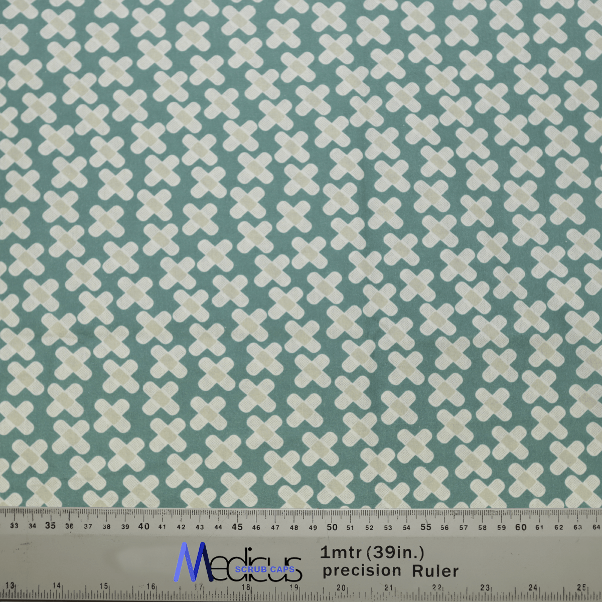 The Hospital Plasters Scrub Cap by Medicus Scrub Caps features a teal background with white plus signs. At the bottom, a measuring ruler labeled 1mtr (39in) precision Ruler in blue and black, ideal for healthcare professionals designing reusable scrub caps.