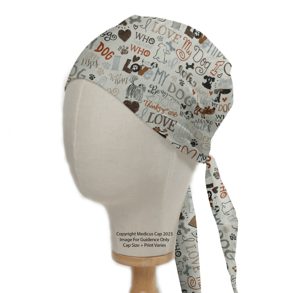 The I Love My Dogs Scrub Cap by Medicus Scrub Caps is perfect for veterinary professionals. This reusable cap, displayed on a mannequin head, showcases dog-themed prints with phrases like Woof in brown and gray, featuring ties that elegantly drape down the back.
