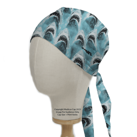 The Jaws Scrub Cap by Medicus Scrub Caps is shown on a mannequin head, boasting a sustainable design with sharks on a blue background and long ties at the back.