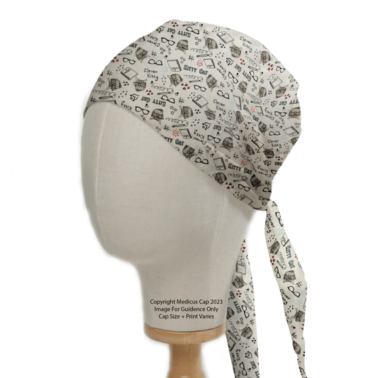 A mannequin head displays a Medicus Scrub Caps Kitty Cat Homework Scrub Cap, featuring medical symbols like stethoscopes and hearts. Eco-friendly and designed for healthcare professionals, it ties neatly at the back and sits on a wooden stand.