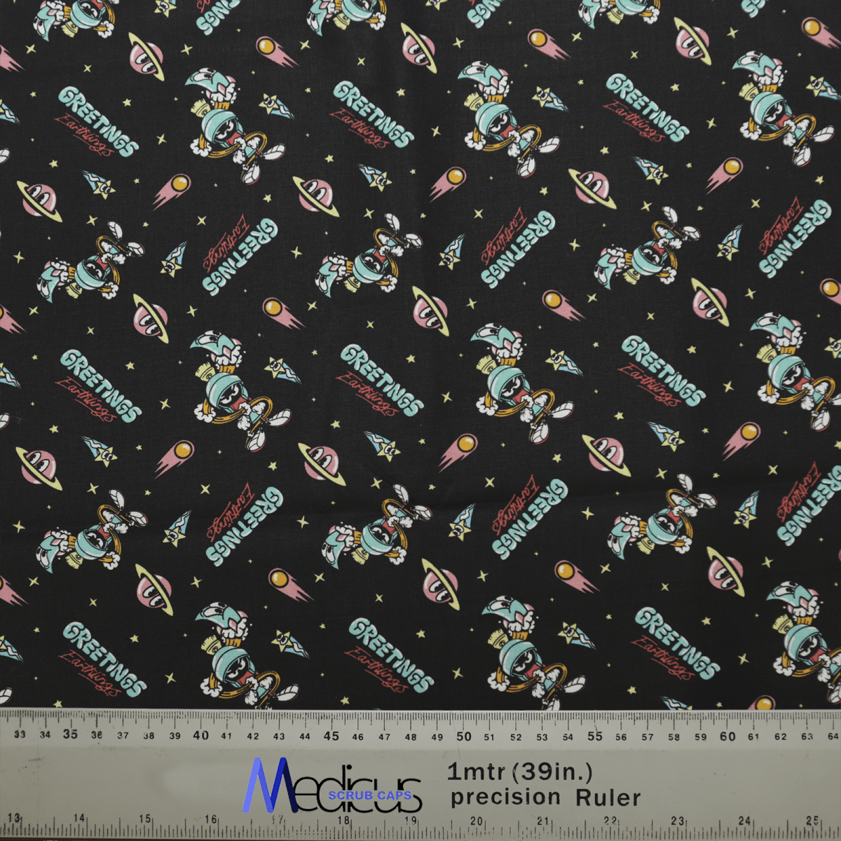 Looney Tunes Marvin the Martian Scrub Cap by Medicus Scrub Caps features Greetings Earthling and UFO designs on black, with rockets, stars, and planets. A 1-meter ruler is visible at the bottom.