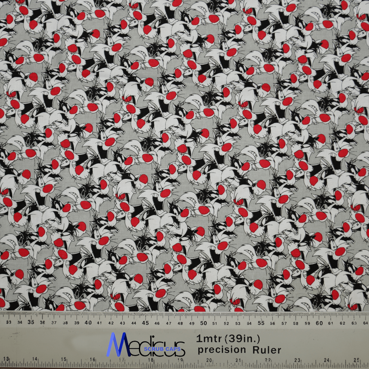 The Medicus Looney Tunes Sylvester Scrub Cap fabric features a dense white and black leaf pattern with red cherries on gray, perfect for crafting and ideal for eco-conscious healthcare professionals. A ruler at the bottom shows measurements in inches and meters.