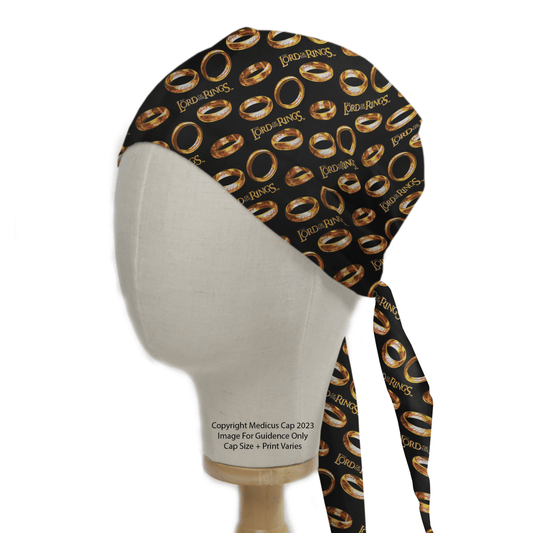 A mannequin head displays the Lord Of The Rings - Golden Rings Scrub Cap by Medicus Scrub Caps, featuring a black design with gold rings and Lord of the Rings text. It ties at the back and includes a 2023 copyright notice, emphasizing its sustainable style.