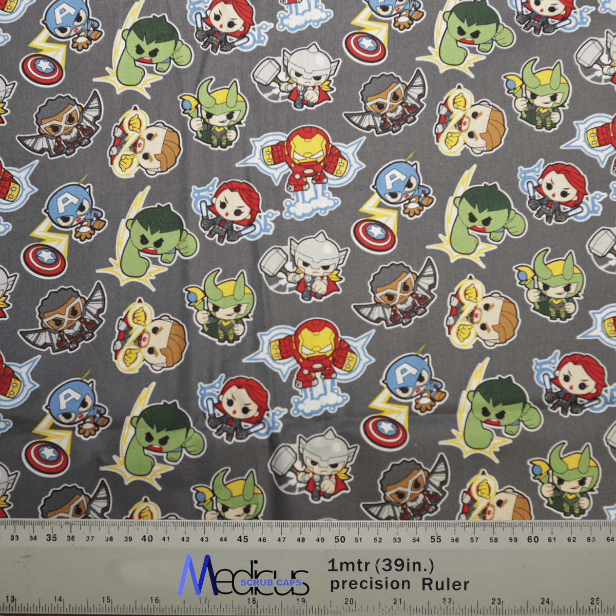 Marvel Avengers Cartoon Fight #2 Superhero Scrub Cap by Medicus Scrub Caps features patterned fabric with superhero characters, symbols on gray background, and Marvel Avengers in costumes with capes and masks. Ideal for honoring healthcare heroes. Includes measurement markings at the bottom.