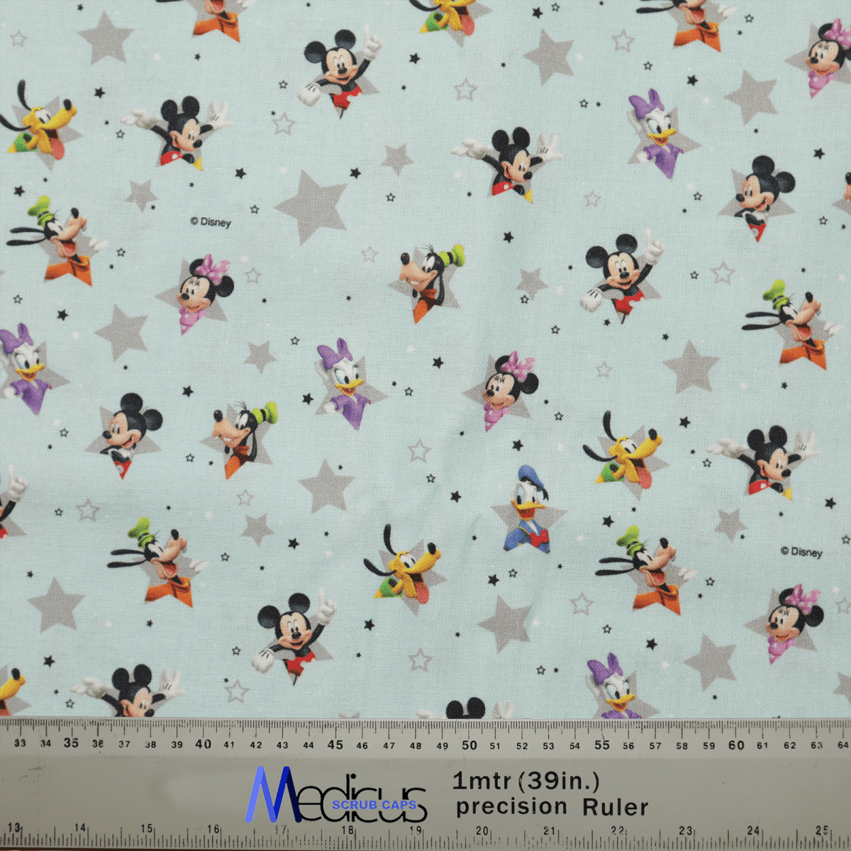 Mickey + Friends Blue Grey Stars fabric, from Medicus Scrub Caps, showcases Mickey & Friends with stars on a light blue background, ideal for crafting healthcare attire like a scrub cap. A ruler at the bottom provides scale in inches and centimeters.