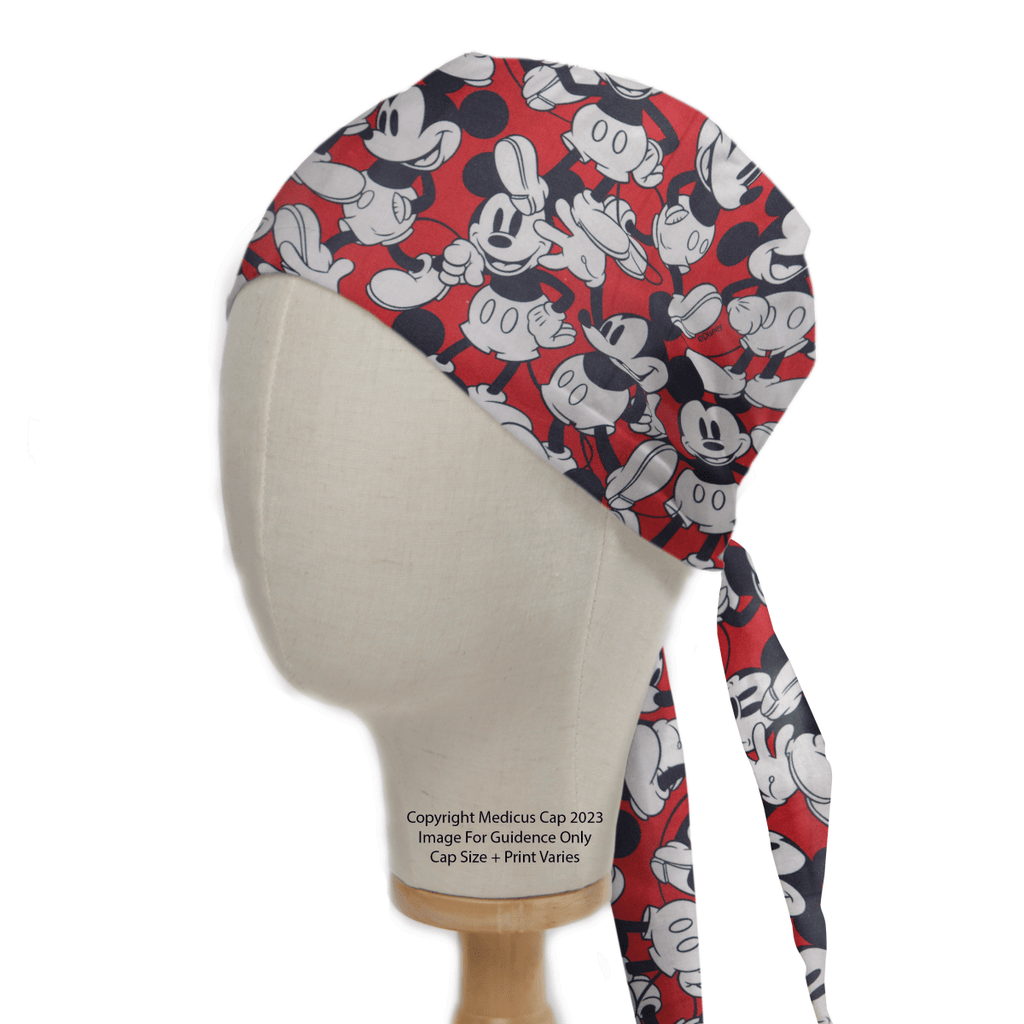 Displayed on a wooden stand, the mannequin head features Medicus Scrub Caps Mickey On Red Scrub Cap, with a black and white design. This cap is ideal for healthcare professionals and ties at the back.