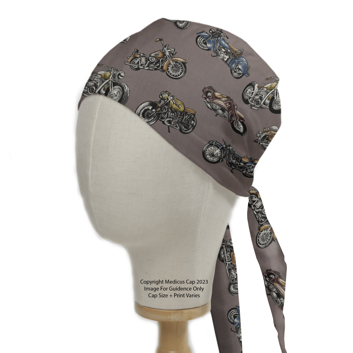 A mannequin head displays the eco-friendly Motorbike Vintage 1950 Scrub Cap by Medicus Scrub Caps, featuring classic motorcycle illustrations on a gray background. The high-quality cap ties at the back and rests on a sturdy wooden base, ideal for motorcycle enthusiasts.