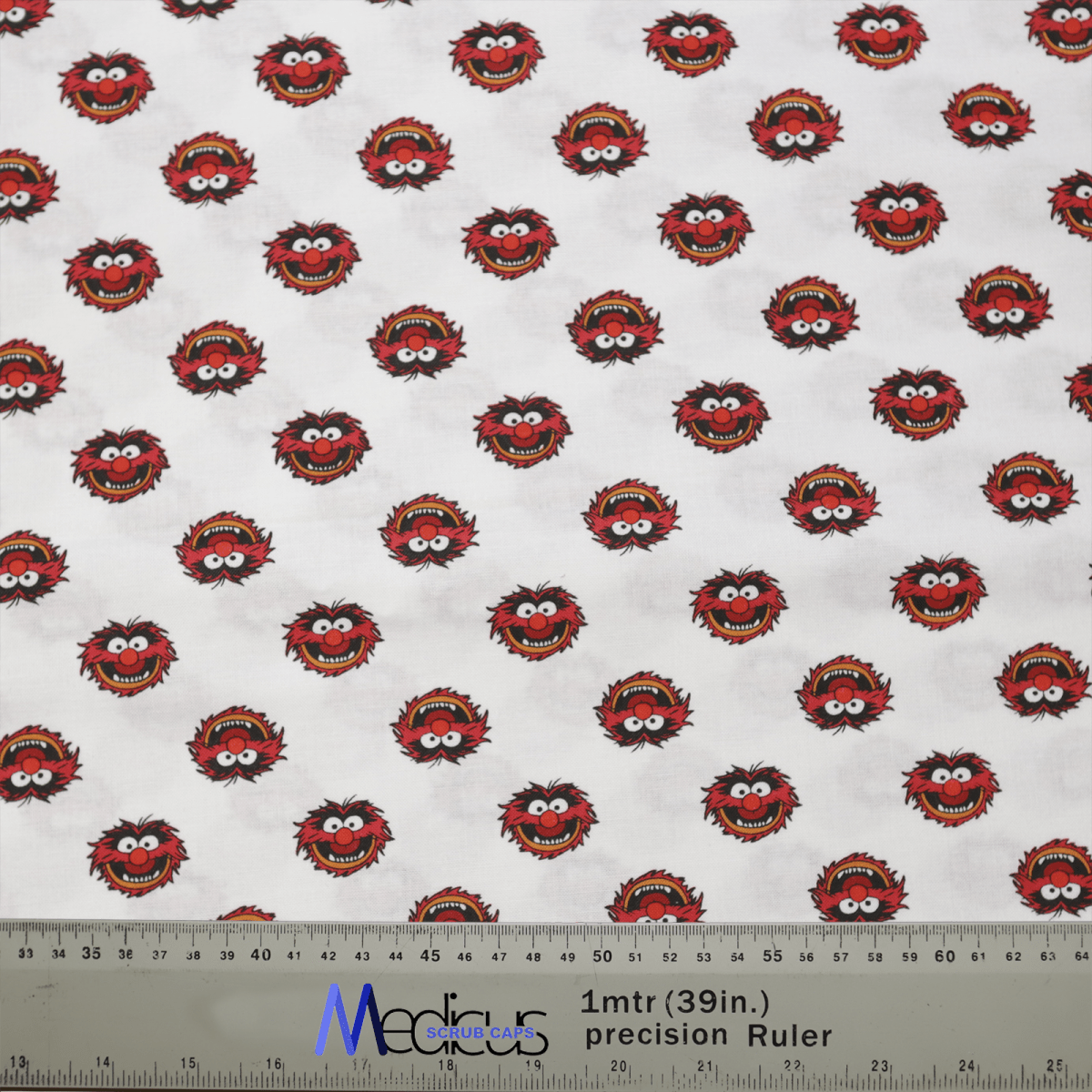 The Medicus Scrub Caps Muppets Animal Toss showcases small red monster faces with wild hair and wide eyes on a white backdrop. Ideal for adding fun to medical attire, this design includes a ruler at the bottom showing measurements in meters and inches for comfort.