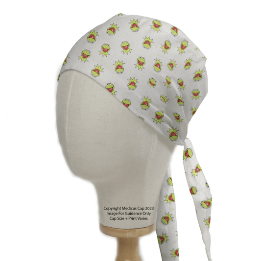 The Muppets Kermit Toss Scrub Cap by Medicus Scrub Caps, shown on a mannequin head, is an eco-friendly white headscarf adorned with green cartoon frog faces. It has a long tail tied at the back and makes for a playful and distinctive medical workwear accessory.