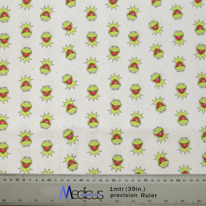 Introducing the eco-friendly Medicus Scrub Caps Muppets Kermit Toss Scrub Cap, crafted from white fabric with a playful pattern of cartoonish green frog faces featuring wide-open mouths and surprised expressions. The design is evenly spaced, with measures in inches and centimeters at the bottom.