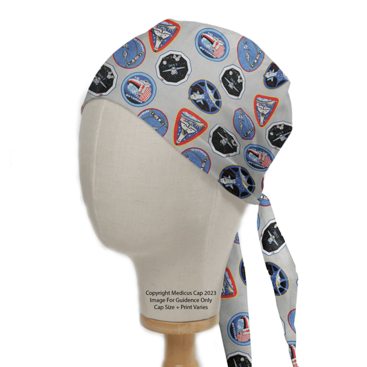 A mannequin head models the NASA Logos Scrub Cap by Medicus Scrub Caps, featuring colorful mission patches on a gray base. The cap ties at the back and embodies NASAs adventurous spirit with vibrant designs.