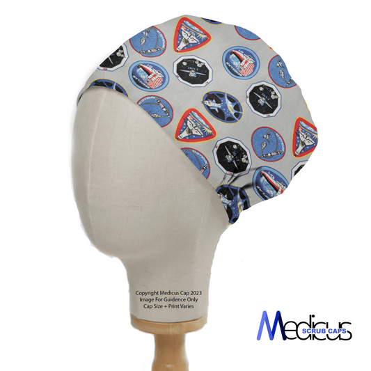 A mannequin head displays the NASA Logos Scrub Cap by Medicus Scrub Caps, featuring NASA logos, space-themed patches, and spacecraft emblems on a gray background. The Medicus Scrub Caps logo appears in the bottom right corner.