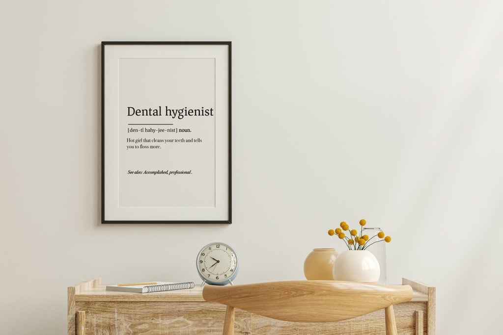 A minimalist workspace showcases Medicus Scrub Caps and a Dental Hygienist Definition Poster on the wall. Below, a wooden desk holds a clock, pen, and vase with yellow flowers. A wooden chair is in front.