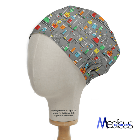 Displayed on a mannequin head, the Science Bunsen Burners Scrub Cap by Medicus Scrub Caps showcases vibrant medical-themed illustrations on a gray eco-friendly fabric, featuring stethoscopes, pills, and syringes. The brands logo appears at the bottom right.