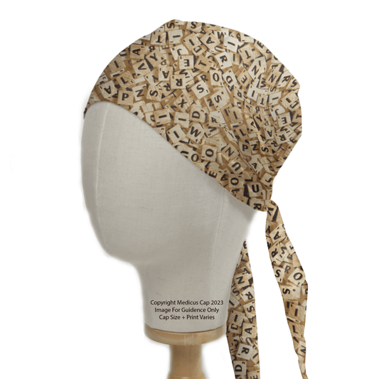 The mannequin head wears the Medicus Scrub Caps Scrabble Letters Scrub Cap, showcasing a sustainable design with a tie back and inclusive style featuring beige fabric adorned with scattered black letters like crossword puzzles.