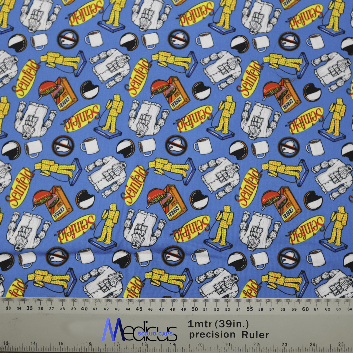 The Medicus Scrub Caps Seinfeld Breakfast Blue Scrub Cap is made from sustainable blue fabric featuring astronaut and rocket illustrations with explore in vivid yellow and red. A grey ruler marked with 39 in and 1 m is shown for scale. Ideal for healthcare professionals.