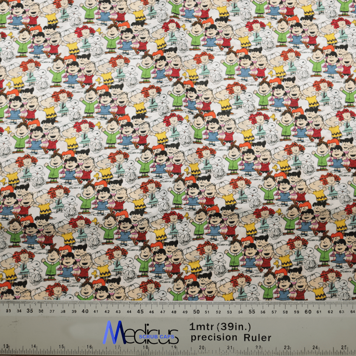 The Snoopy Charlie Brown + Friends Scrub Cap from Medicus Scrub Caps features an eco-friendly fabric with vibrant stripes, zigzags, and cartoon characters like Snoopy and Charlie Brown. A ruler measures 1 meter (39 inches), perfect for creating unique scrub caps or other crafty projects.