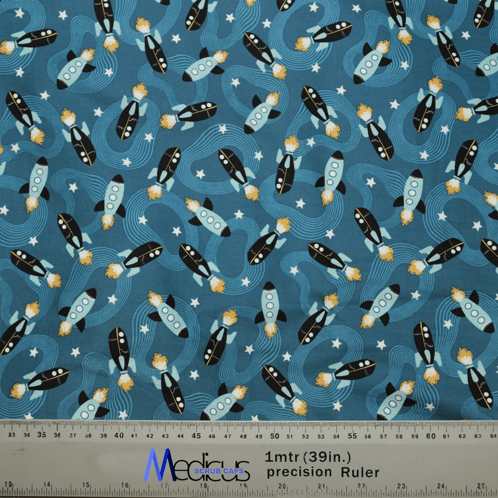 This Medicus Scrub Caps fabric features black and white rockets with orange flames, blue windows on a starry blue background, ideal for crafting a Space Ships Scrub Cap. Includes a 1-meter (39 inches) ruler at the bottom. Perfect for healthcare professionals.